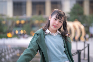 A charming young girl in a green coat poses outdoors in an elegant urban setting with a blurred bokeh background of golden lights, exuding a warm and lively personality in a serene atmosphere.