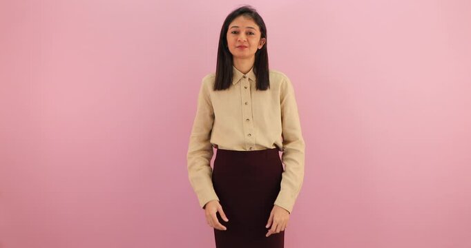 Happy young asian woman fix hair, looking and smiling at camera isolated over pink background.