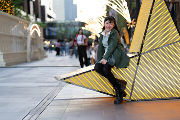 Obraz premium A joyful young girl in a green coat making playful expressions, standing against a backdrop of golden bokeh lights and tall buildings, capturing a fun and lively festive spirit.