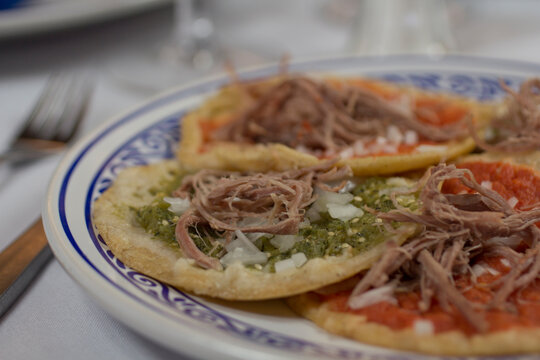 Close-up of a single green chalupa poblana with jalape&ntilde;o salsa, served on a Talavera plate. A classic Mexican street food favorite.