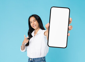 Beautiful Asian woman holding big smartphone mockup of blank screen and smiling on blue background.