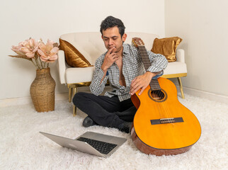 In a cozy home setting, a musician combines technology and tradition, studying online while his acoustic guitar stands ready for practice.