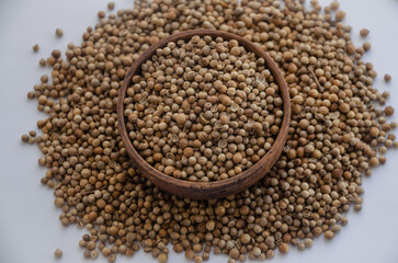 Whole coriander grain in a wooden plate and scattered around the edges