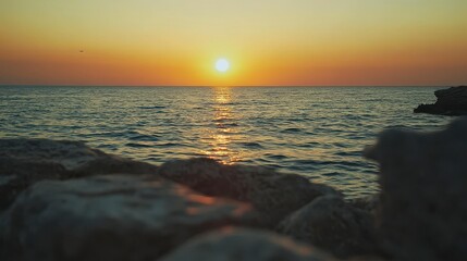 Serene Sunset Over Calm Ocean Waves with Warm Orange and Yellow Skies Reflecting on Water Surface by Rocky Shoreline in Tranquil Coastal Environment