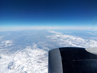 Window view of airplane flying over snowy mountains of Vancouver Canada in winter time with cold,...