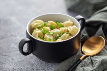 Homemade boiled dumplings or pelmeni with broth and scallion in a ceramic bowl on the table.