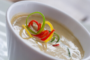 Close-up of vibrant organic zucchini pumpkin soup topped with thin slices of red, yellow, and green bell peppers.
