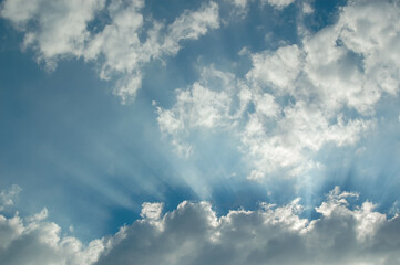 Sun rays stretch from behind clouds in a blue sky on a sunny day