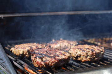 Juicy beef patties grilling over flames with smoke rising