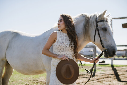 Woman in hat with white horse on ranch on sunny day