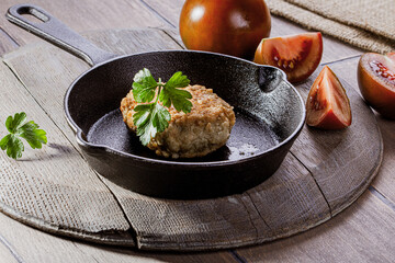 Cast iron frying pan with fried cutlet and tomatoes on wooden table
