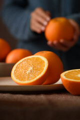 Fresh navel orange fruit on brown ceramic plate with woman in green dress holding one orange.