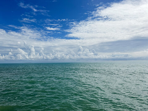 Calm rippled sea and white clouds in blue sky.