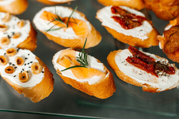 various types of canapés on baguette slices. One of the canapés has what looks like cream cheese spread on it, topped with pieces of smoked salmon and a sprig of rosemary.