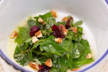 Fresh sautéed arugula with toasted pecans and dried cranberries in a rustic bowl.