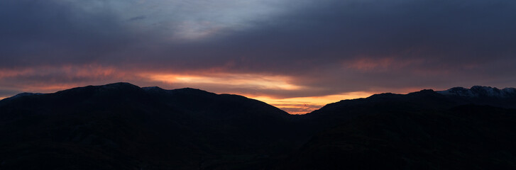 Large panorama landscape image of mountains at sunset with colorful vibrant sky and silhouetted mountain range