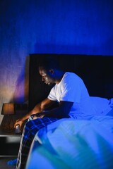 Fototapeta premium Worried man with a beard in bed. Sleepless young male looking pensive in a cozy bedroom with soft lighting