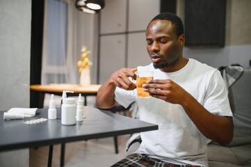 African American man sick with flu or cold at home. He takes medicine and drinks tea