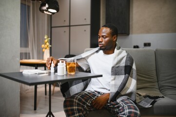 African American man sick with flu or cold at home. He takes medicine and drinks tea