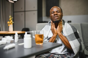 Man experiencing sore throat pain while sitting on couch in living room.