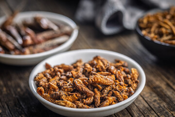 Dried salted insect. Roasted crickets in bowl on wooden table.