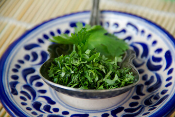 A silver spoon full of chopped cilantro over a authentic mexican Talavera clay plate, high angle view close-up.