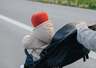 Close up of young mother in warm coat pushing baby stroller and slowly crossing street on...