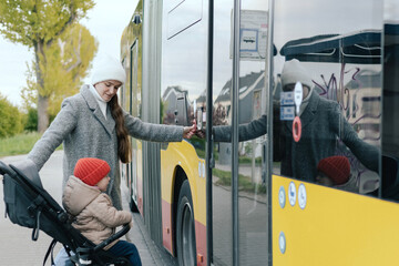 Mother with baby carriage getting into a bus on the station. Woman with stroller in the city. Low-floor bus. Close-up. The concept of solo parenting and city transport.