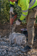 Obraz premium A worker smashes a large concrete block using an electric demolition hammer