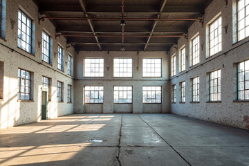 Photograph of a large, sunlit industrial warehouse with white brick walls, large grid windows, and a wooden ceiling.