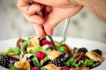 Hands of a chef preparing a grilled chicken salad bowl, close-up.