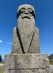 Symmetric view of a statue of a poet with a long beard and glasses, captured on a clear sunny day.