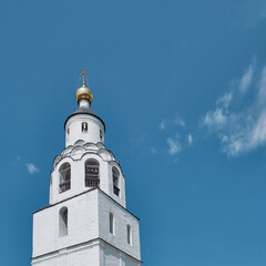 Fototapeta premium White Orthodox church bell tower with golden dome and cross. Traditional Russian architecture.