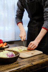Unrecognizable man in a dark apron skillfully chops fresh celery on a wooden cutting board