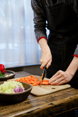 Unrecognizable man is chopping vibrant carrots on a wooden cutting board