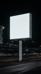 A vertical blank white billboard stands in a city street at night, illuminated against a dark urban backdrop.