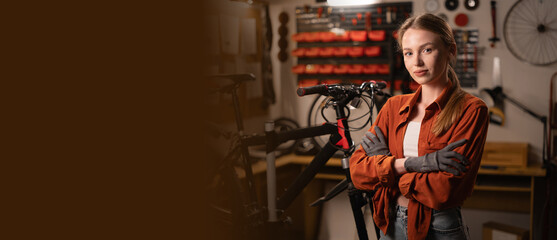 Portrait of cute repairwoman in bicycle shop with arms crossed. Bike mechanic in cycling workshop.