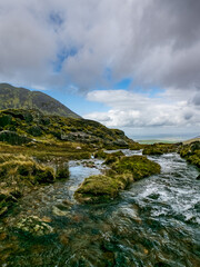 Fototapeta premium Water rushes over stones in a narrow mountain valley. The surrounding hills are sparsely vegetated.