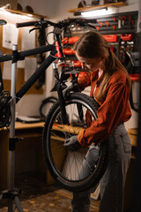 Attractive experienced female bicycle repairman repairs and repairs a mountain bike standing on a...