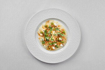 A fresh and healthy seafood dish featuring a delicate piece of white fish carpaccio, surrounded by a colorful array of fresh vegetables