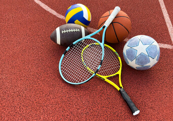 A variety of sports equipment including an american football, a soccer ball, a tennis racket, a...