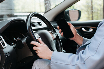 Close-up of woman's hands holding the steering wheel and using cell phone, the concept of safe...