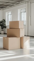 Four large cardboard boxes are stacked neatly in a bright, minimalistic warehouse space with natural lighting and a potted plant in the background.