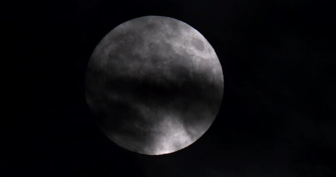 Footage of the full moon moving through the clouds at night.