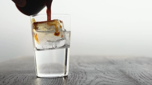 Slow motion making espresso tonic in tumbler glass, pour espresso in tonic with ice cube
