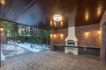 Exclusive design of an outdoor terrace with a barbecue oven. Beautiful lighting. Winter .snow-covered landscape, paths illuminated by street lights.