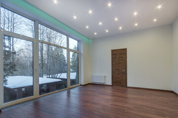 A room in a country house, with final finishing, unfurnished. Panoramic window with a view of the courtyard on a winter evening.