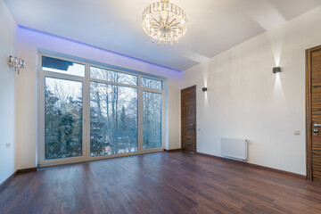 Obraz premium Panoramic window in the room of a luxurious country mansion with a picturesque view of .the winter landscape. A room with a parquet floor, a luxurious chandelier, unfurnished.