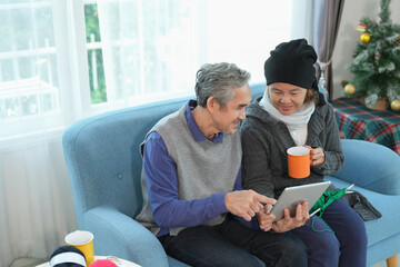 senior married couple sitting on couch,woman holding cup of hot drink learning to knit on tablet that a man holding tablet and talking together