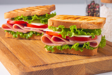 Close-up of two sandwiches with bacon, salami, prosciutto and fresh vegetables on rustic wooden cutting board. Club sandwich concept